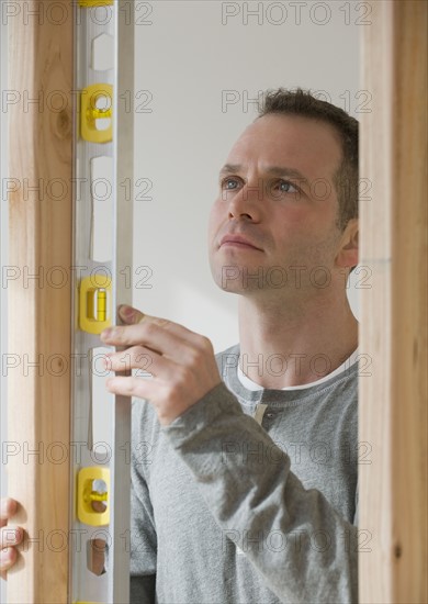 Man holding level next to wooden stud.