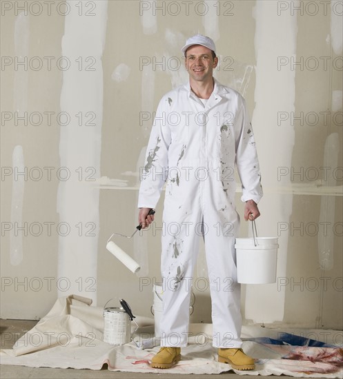 Male painter holding paint roller and paint can.