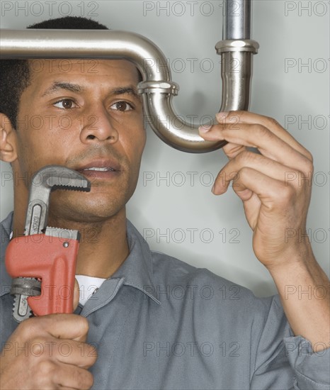 African male plumber holding wrench next to pipe.