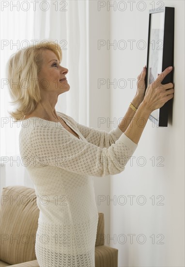 Senior woman hanging picture on wall.