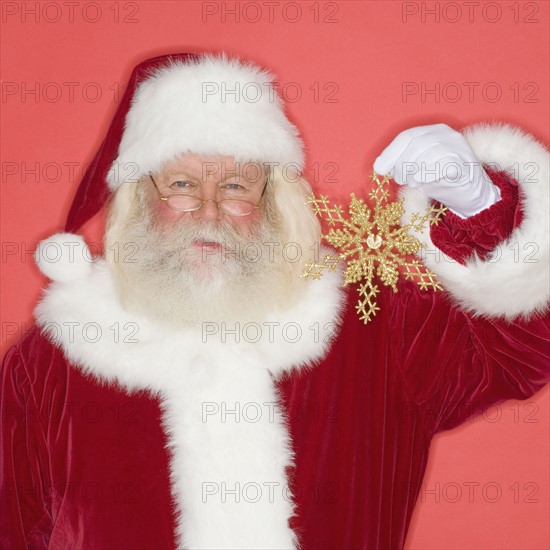 Santa Claus holding snowflake Christmas ornament.