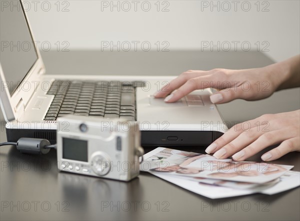 Digital camera and photographs next to laptop.