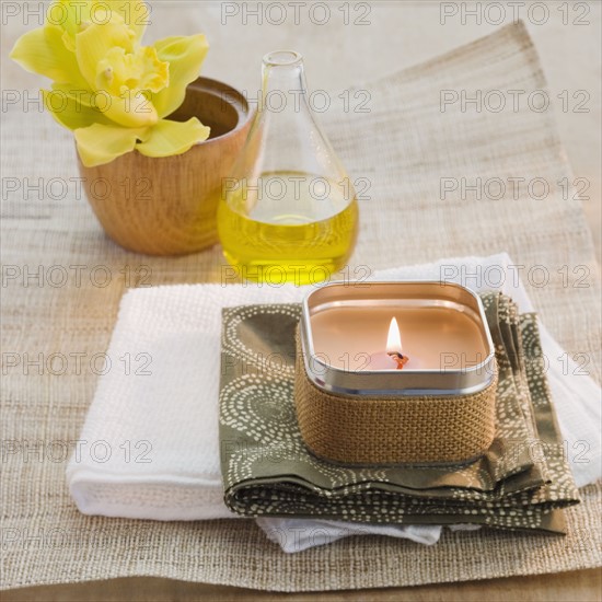 Lit candle in front of flower and bath oil.