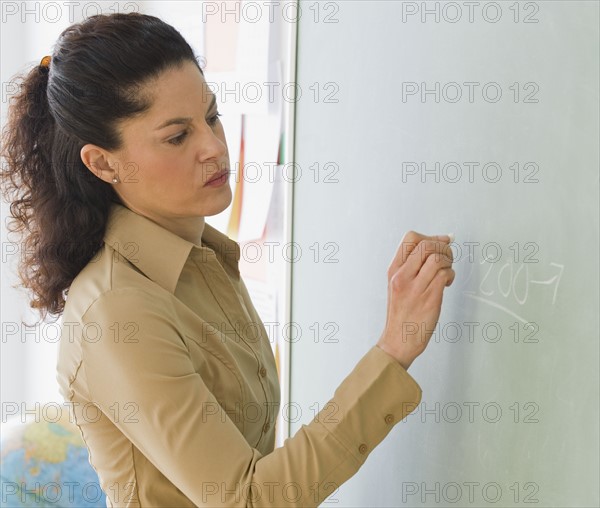 Hispanic teacher writing on blackboard.