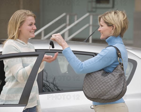 Mother handing car keys to teenaged daughter.
