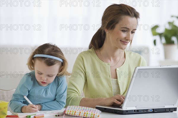 Mother working next to daughter coloring.