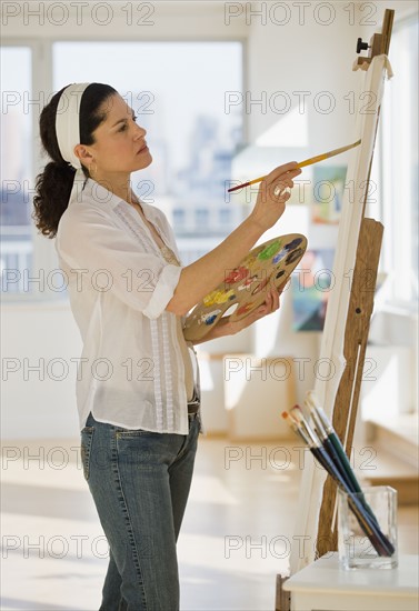 Hispanic woman painting on easel.