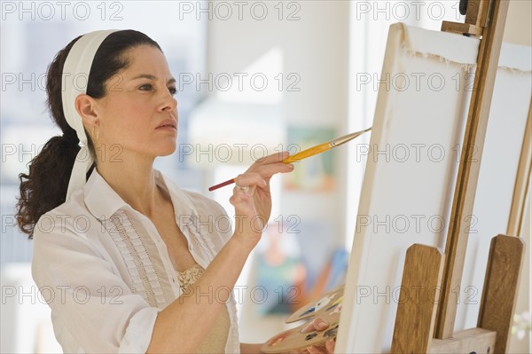 Hispanic woman painting on easel.