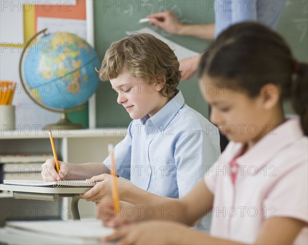 Multi-ethnic children writing at school desks.