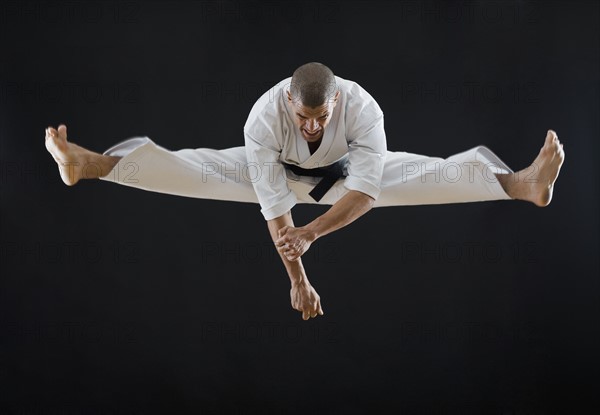 Hispanic male karate black belt jumping in air.