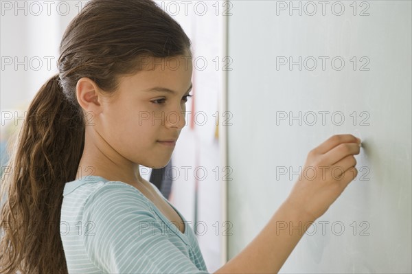 Hispanic girl writing on blackboard.