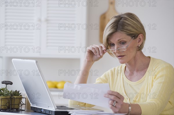 Woman reading mail next to laptop.