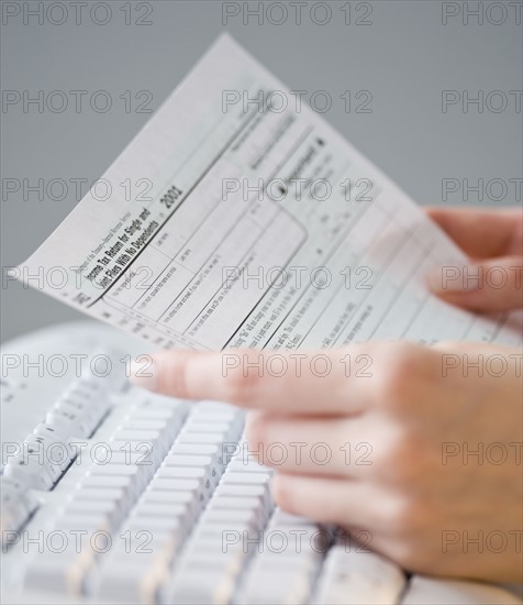 Woman holding tax form over keyboard.