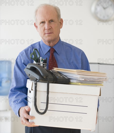 Senior businessman carrying box of office items.