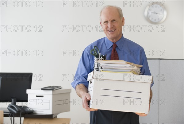 Senior businessman carrying box and office supplies.
