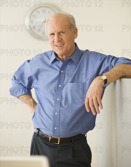 Senior businessman leaning on cubicle wall.