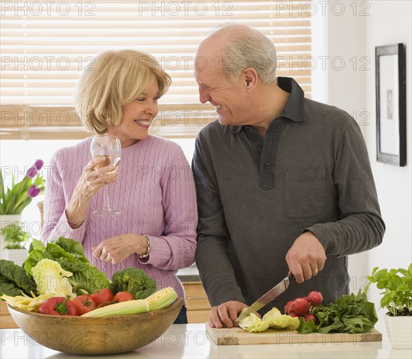 Senior couple chopping vegetables and drinking wine.