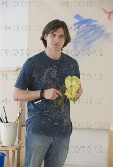 Man cleaning paintbrush in front of easel.