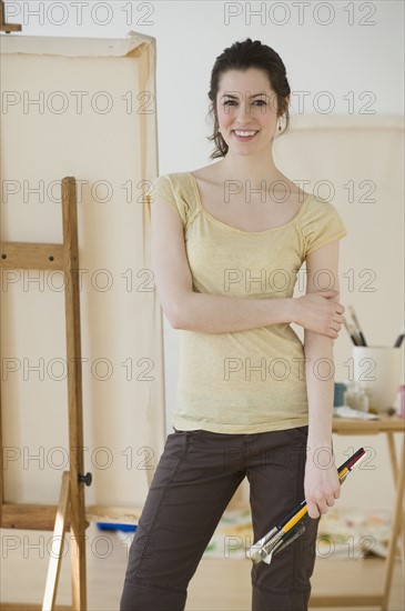 Woman holding paintbrushes in front of easel.