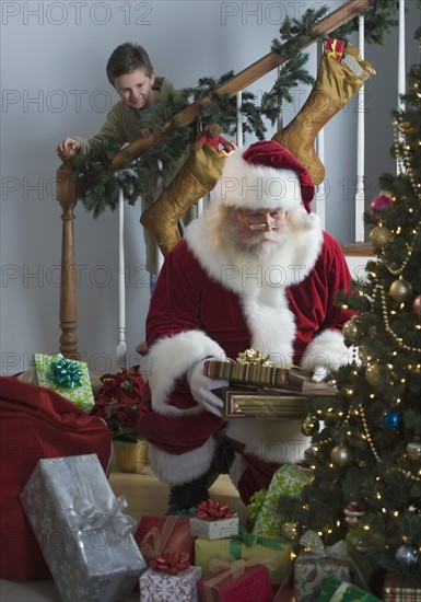 Boy watching Santa Claus leave gifts under Christmas tree.