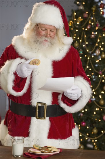 Santa Claus reading letter and eating cookies.