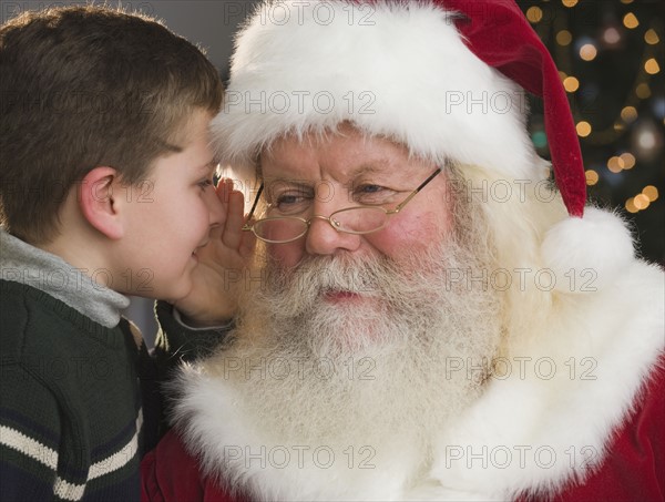 Boy whispering in Santa Claus’s ear.