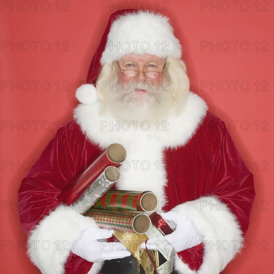 Santa Claus holding wrapping paper and ribbon.