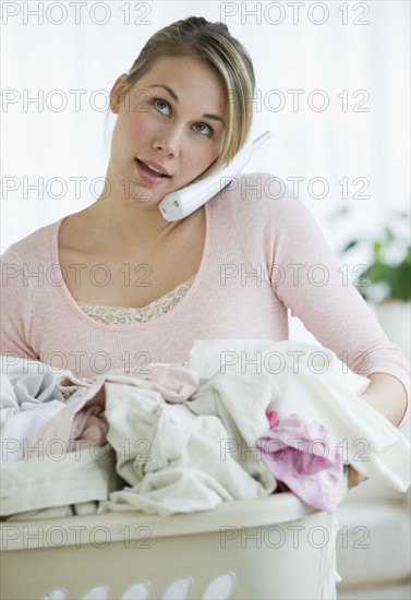 Woman with laundry basket talking on telephone.