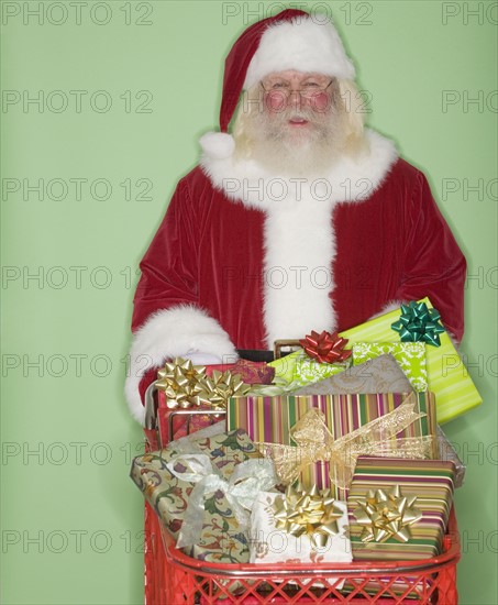 Santa Claus pushing shopping cart of gifts.