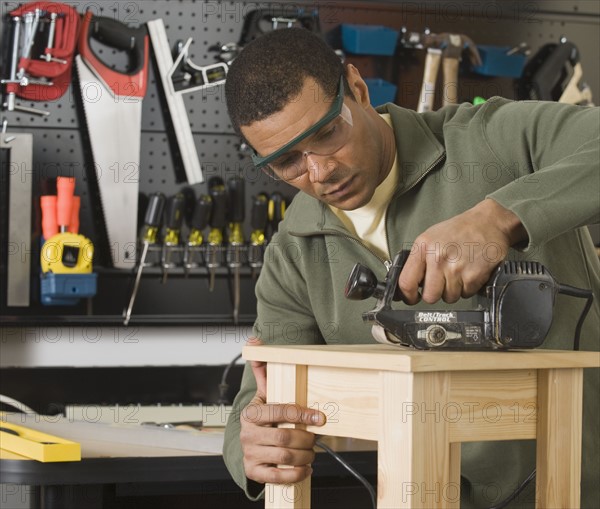 African male woodworker sanding table.