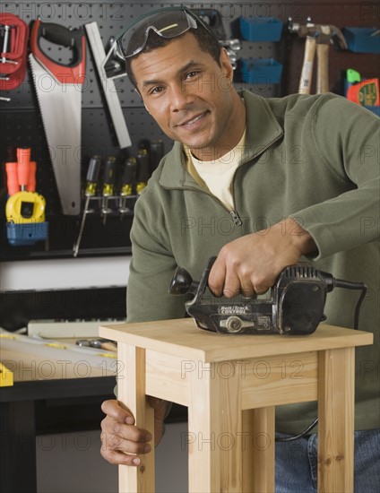 African male woodworker sanding table.