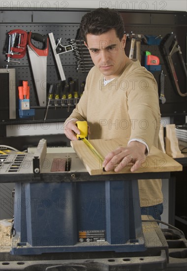 Male woodworker measuring piece of wood.