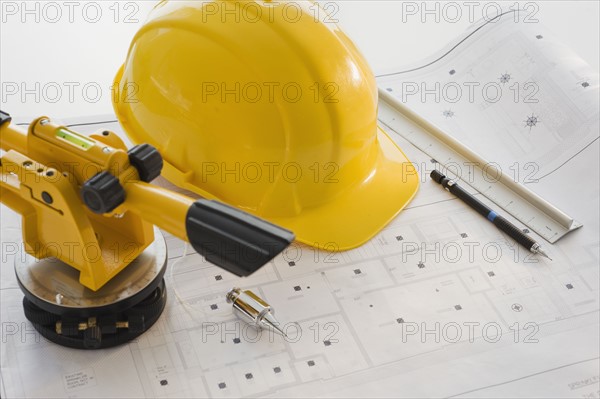 Hard hat and surveying equipment on blueprints.