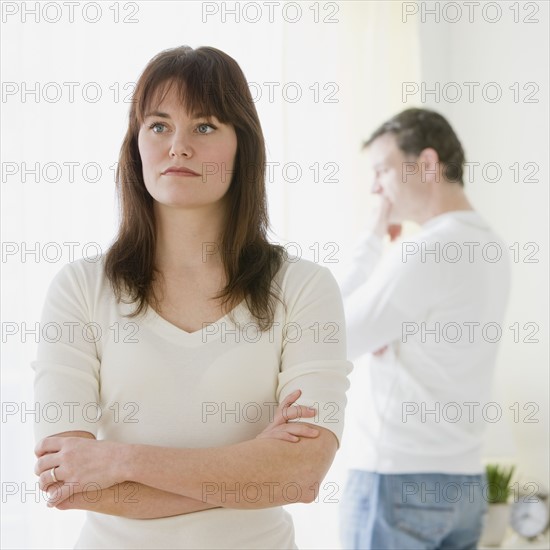 Woman with arms crossed and husband in background.