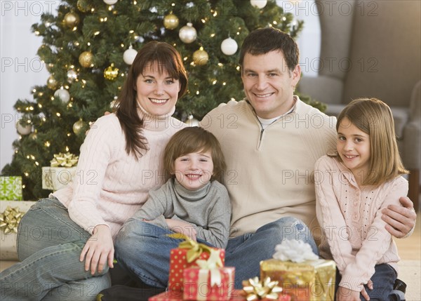 Family hugging in front of Christmas tree.