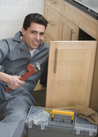 Male plumber holding wrench next to sink.