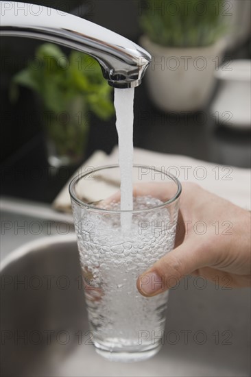 Man filling glass of water at sink.