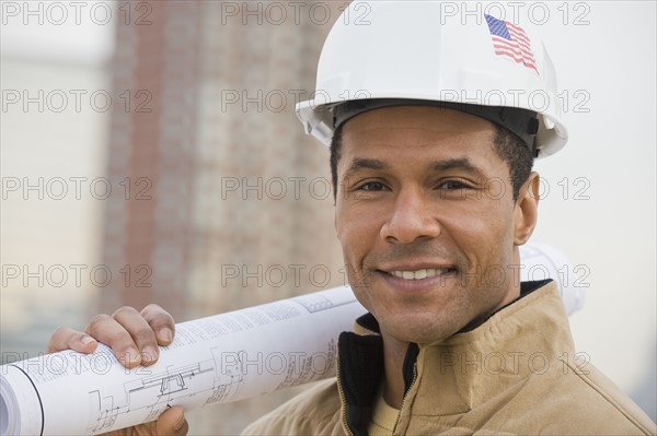 African male construction worker holding blueprints.