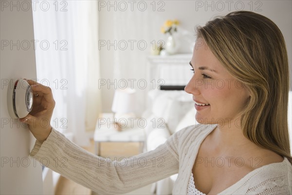 Woman adjusting thermostat.