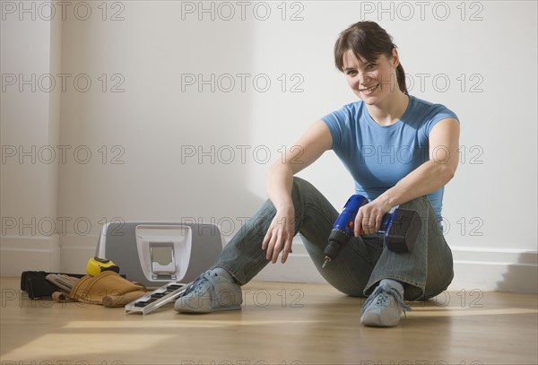 Woman sitting on floor holding cordless drill.