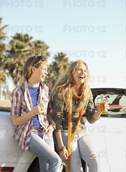 Two women drinking beer next to convertible. Date : 2008