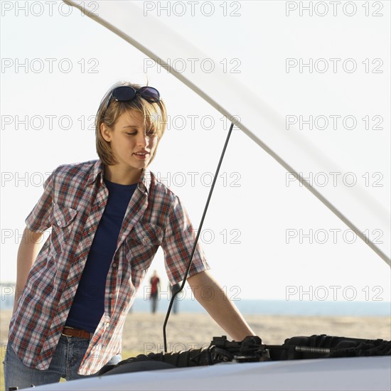 Woman looking under car hood. Date : 2008