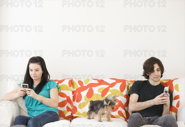 Man and woman dialing cell phones on opposite ends of sofa. Date : 2008