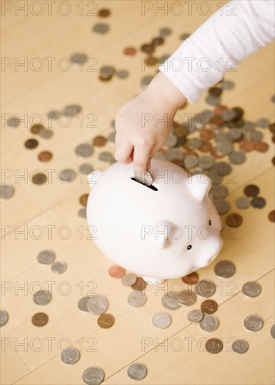 Child putting coin in piggy bank. Date : 2008
