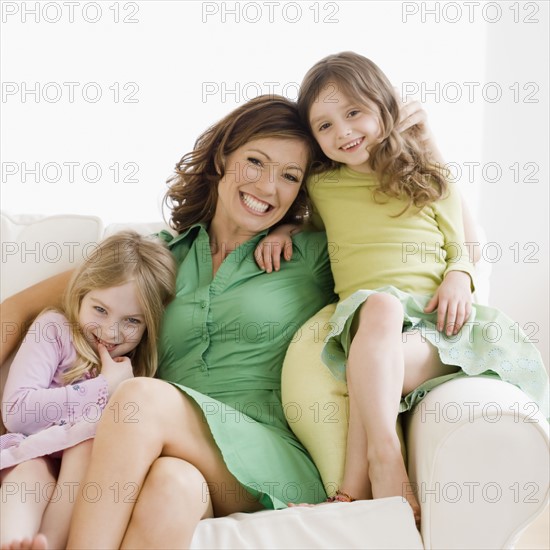 Mother and daughters hugging on sofa. Date : 2008