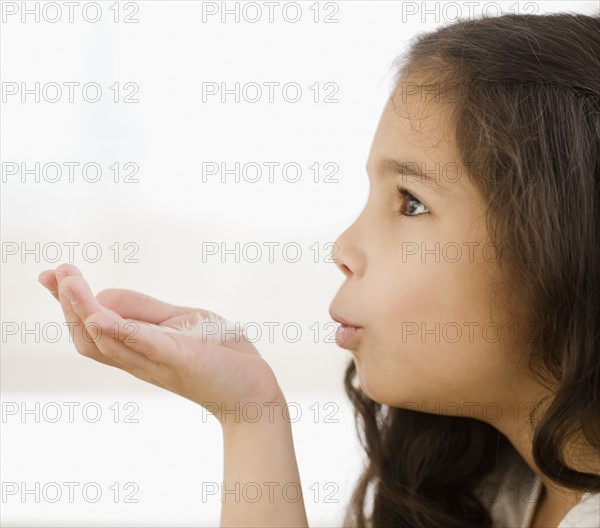 Hispanic girl blowing on feather in hand. Date : 2008