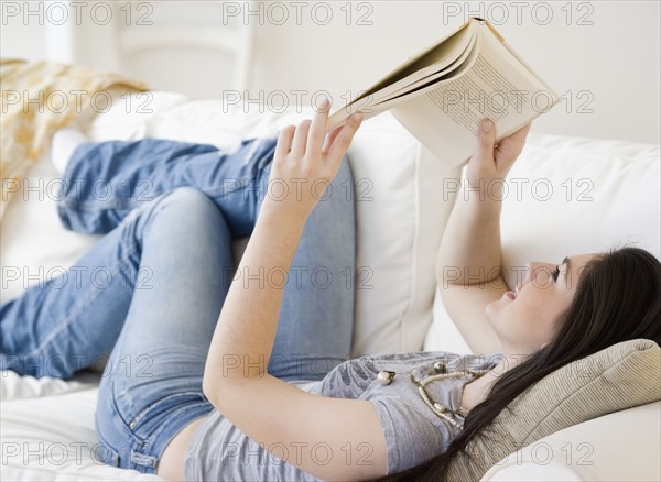 Woman reading book on sofa. Date : 2008