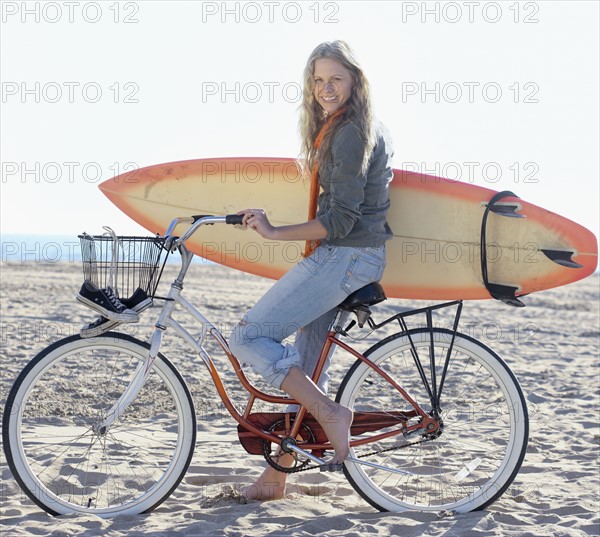 Woman with bicycle and surfboard on beach. Date : 2008