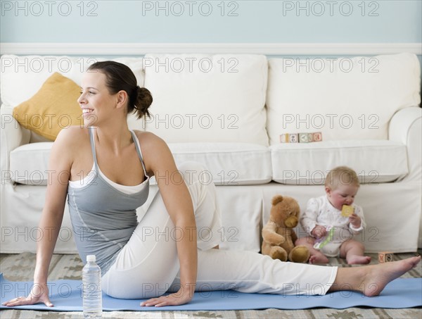 Mother practicing yoga next to baby on floor. Date : 2008