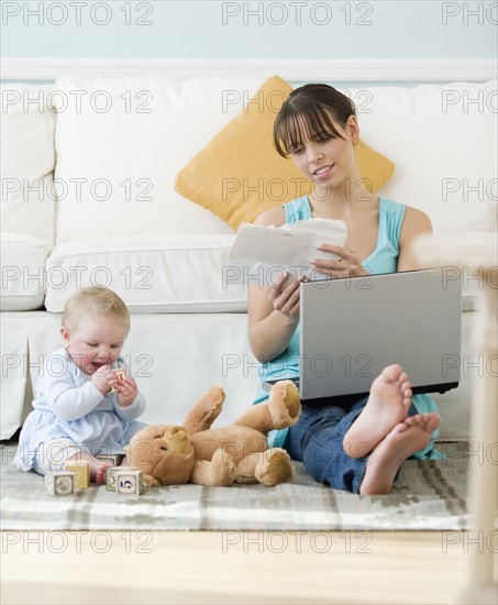 Mother working next to baby playing on floor. Date : 2008